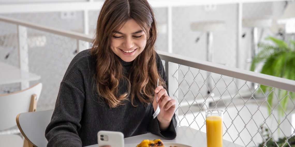Adolescente comiendo con el celular (Freepick/pvproductions).