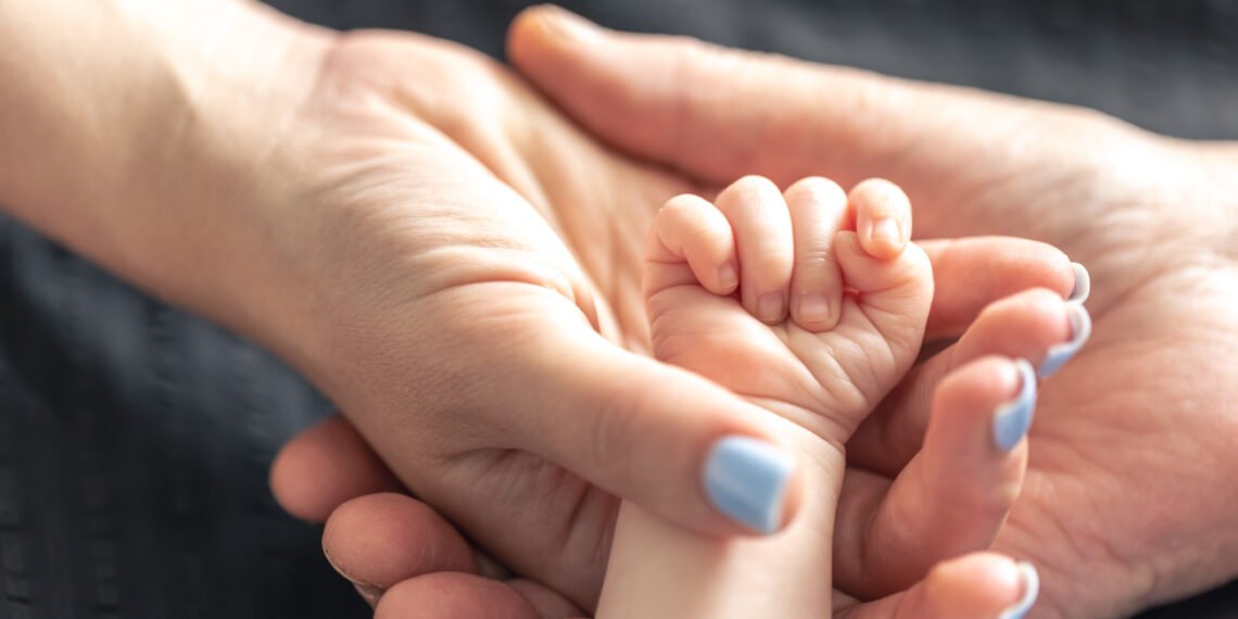 Adopción. Padres sosteniendo la mano de un bebé (pvproductions/FreePick).