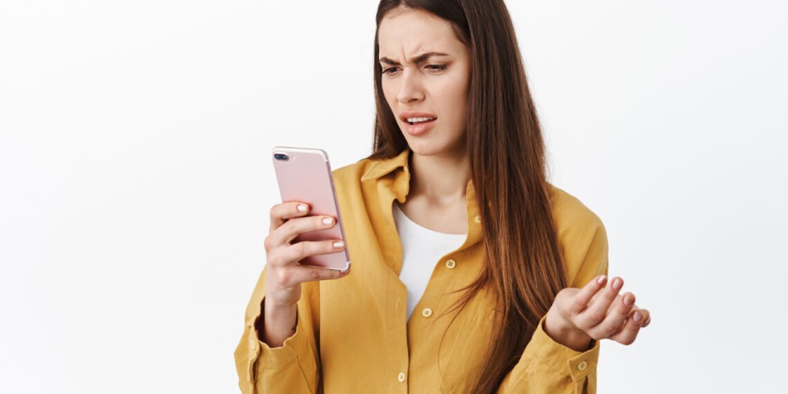 Joven confundida usando el celular (Cookie_Studio/Magnific).