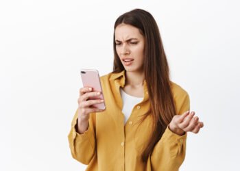 Joven confundida usando el celular (Cookie_Studio/Magnific).
